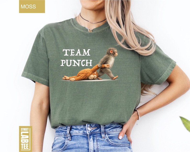 May include: Moss green t-shirt with the text "TEAM PUNCH" in white. The shirt features a cartoon illustration of a monkey pulling another monkey. The shirt is made of a soft, comfortable material.
