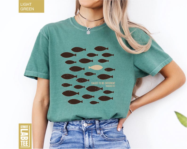 Puede incluir: Camiseta verde claro con un dise&ntilde;o de peces marrones y el texto "CALLED TO BE DIFFERENT" y "ROMANS 12:2". Un estilo casual y c&oacute;modo.