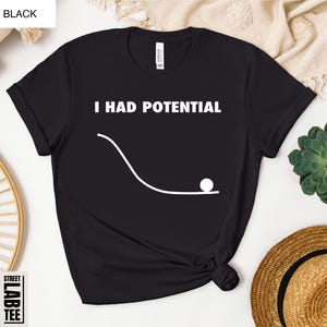 May include: Black t-shirt with the text "I HAD POTENTIAL" above a white graphic of a ball rolling down a curved line. The shirt is a crew neck and has a Street Lab Tee label.