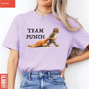 May include: A light purple t-shirt with the text "TEAM PUNCH" above a graphic of two monkeys. One monkey is pulling the other by the arm. The shirt is a casual style.