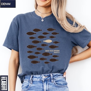 Puede incluir: Camiseta azul denim con un gr&aacute;fico de peces. El dise&ntilde;o presenta varios peces marrones nadando en una direcci&oacute;n, con un pez beige nadando en la direcci&oacute;n opuesta. El texto en la camiseta dice "CALLED TO BE DIFFERENT ROMANS 12:2".