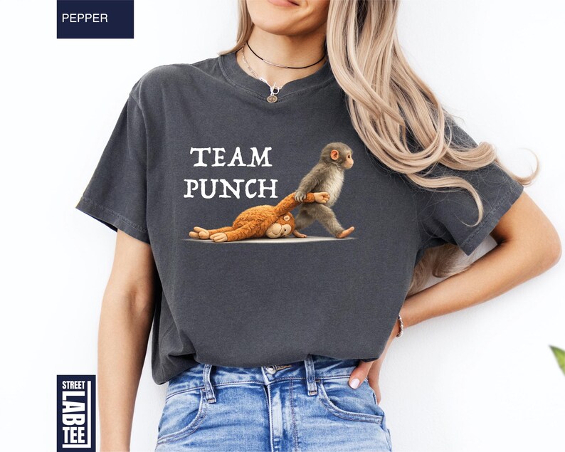 May include: Dark gray t-shirt with the text "TEAM PUNCH" in white. The shirt features a cartoon illustration of two monkeys, one standing and the other lying down. The shirt is a comfortable, casual style.