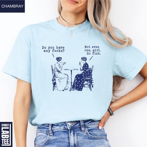 May include: Light blue t-shirt with a navy blue graphic of two women seated at a table, with the text "Do you have any fucks?" and "Not even one, girl. Go fish."