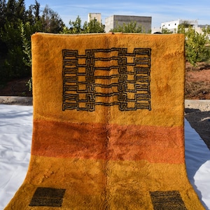 May include: A yellow and orange handwoven rug with a black geometric pattern. The rug has fringe on the bottom edge.