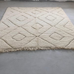 May include: A white, fluffy rug with a diamond pattern woven into the fabric. The rug has a fringe border.