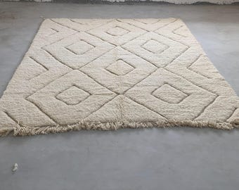 Op de afbeelding: Een wit, pluche vloerkleed met een ruitpatroon dat in de stof is geweven. Het vloerkleed heeft een franje rand.