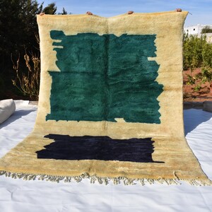 May include: A hand-woven rug with a cream background and abstract geometric designs in shades of green and black. The rug has a fringe border.