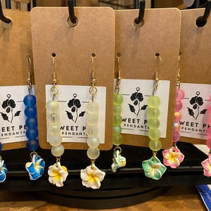 May include: Four pairs of earrings with flower charms. Each pair features a different color of frosted glass beads: blue, white, green, and pink. The earrings are labeled "Sweet Pea Pendants!"