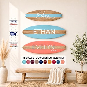 May include: Three wooden surfboard-shaped signs with names in white lettering. The top sign is light blue with "Ethan Matthew", the middle sign is blue with "ETHAN", and the bottom sign is coral with "EVELYN Rose". A bench and rug are in the foreground.
