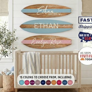 May include: Three wooden surfboard-shaped signs with names in white script. The top sign has a blue stripe and the name "Ethan Matthew". The middle sign says "ETHAN" with a blue stripe. The bottom sign has a pink stripe and says "Evelyn Rose".