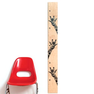 May include: A wooden growth chart featuring three giraffe illustrations. The chart is marked with inch increments from 2 to 6 feet. The giraffe heads peek out from behind the chart's edge, adding a playful touch to the design.