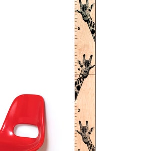 May include: A wooden growth chart featuring giraffe illustrations. The chart has black markings for measuring height in feet and inches, with giraffe faces peeking out from behind the numbers. A red chair is in the lower left corner.