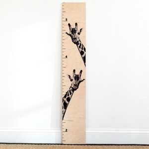 May include: A wooden growth chart featuring a black and white giraffe peeking out from behind the ruler. The ruler is marked with numbers from 2 to 5.