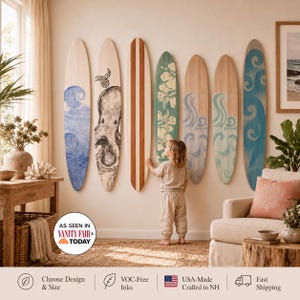May include: Seven decorative wooden surfboards mounted on a wall, featuring various designs including blue waves, an octopus illustration, a central wood-grain stripe, a green hibiscus floral pattern, and swirling blue and teal wave motifs.