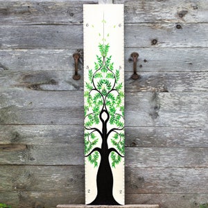 May include: A black and green tree-shaped growth chart with numbers 2, 4, 5, and 6 on the side. The tree is painted on a white wooden board.