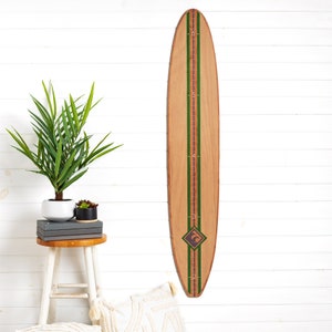 May include: A wooden surfboard-shaped growth chart with a light brown finish. It features green and brown stripes down the center with numbered height markings in inches. A diamond-shaped emblem is near the bottom.