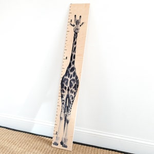 May include: A wooden growth chart featuring a black and white giraffe illustration. The chart has numbers from 2 to 5 printed on it.