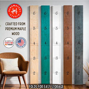 May include: Wooden growth charts in various colors, including natural, teal, white, brown, and gray. Each chart is marked with inch increments from 2 to 6 feet. The text reads "CRAFTED FROM PREMIUM MAPLE WOOD" and "FOLDS FOR EASY STORAGE."