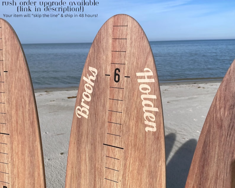 May include: Wooden growth chart rulers with names and height markings. The rulers are made of light brown wood and have white text. The background shows a beach with the ocean and sky.