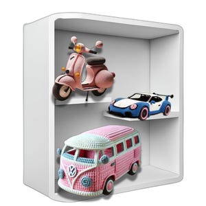 Può includere: Un'unità a scaffale bianca con tre ripiani che mostrano veicoli giocattolo all'uncinetto. Lo scaffale superiore ha uno scooter rosa, lo scaffale intermedio ha un'auto sportiva blu e lo scaffale inferiore ha un furgone Volkswagen rosa e blu.