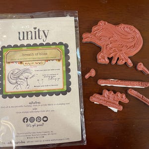 May include: A collection of rubber stamps for crafting, featuring a large floral design and several smaller accent stamps. The packaging includes the text "unity" and "breath of bliss". The stamps are in shades of red and brown.