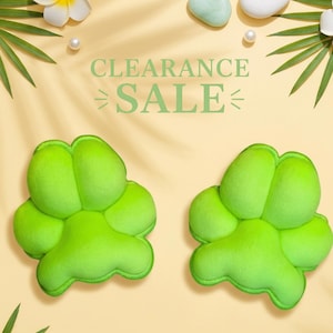 May include: Two bright lime green plush paw-shaped cushions with soft rounded toes and a central pad. The text CLEARANCE SALE is printed in light green in the center above the two paw-shaped items, surrounded by white flowers and palm leaves.