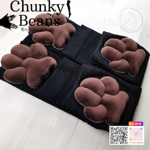 May include: A pair of black knee-high socks with brown paw print designs. The socks are folded and stacked on a light wood surface. The text "Chunky Beans" is visible at the top of the image.