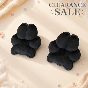 May include: Two black plush paw-shaped cushions with soft velvet-like texture. The text CLEARANCE SALE is printed in dark gray at the top right. The design features four rounded toe pads and a larger central pad, mimicking an animal paw print.