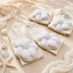 May include: Cream-colored baby socks with a white cloud design. The cloud is made of soft, plush material and is stitched onto the socks. The socks are folded and arranged with seashells and decorative elements, suggesting a baby shower or nursery theme.