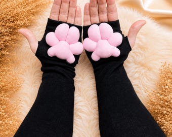 May include: Black fingerless gloves with pink paw pads. The gloves are long-sleeved and made of a soft material. The paw pads are a light pink color and are sewn onto the back of the hand.