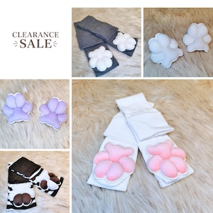 May include: A collection of knee-high socks featuring plush, padded animal paw designs in various colors including white, pink, purple, and brown. Some socks are solid gray, white, or black and white striped, all adorned with soft, raised paw pads.