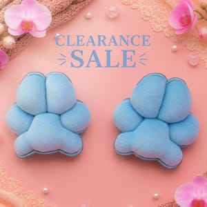 May include: Two light blue plush paw-shaped cushions on a pink background. The text CLEARANCE SALE is printed in blue in the center. The image is decorated with pink orchid flowers, white pearls, and textured fabric accents in the corners.