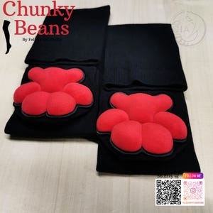 May include: A pair of black socks with a red paw print design. The paw prints are made of a soft, textured material and are outlined in black. The text "Chunky Beans" is in the upper left corner.