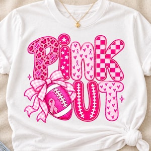 Op de afbeelding: Een wit T-shirt met korte mouwen en de tekst Pink Out in felroze letters. Het ontwerp bevat een football met een roze lint, een geruite strik en patronen van luipaardprint, sterren, hartjes en ruitjes in verschillende roze tinten.