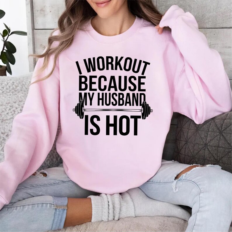 May include: Pink sweatshirt with the text "I workout because my husband is hot" and a black barbell graphic.