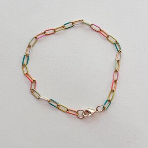 May include: A gold-colored chain bracelet with colorful enamel links in shades of pink, orange, green, and blue. The bracelet has a lobster clasp closure. The jewelry is displayed on a white background.