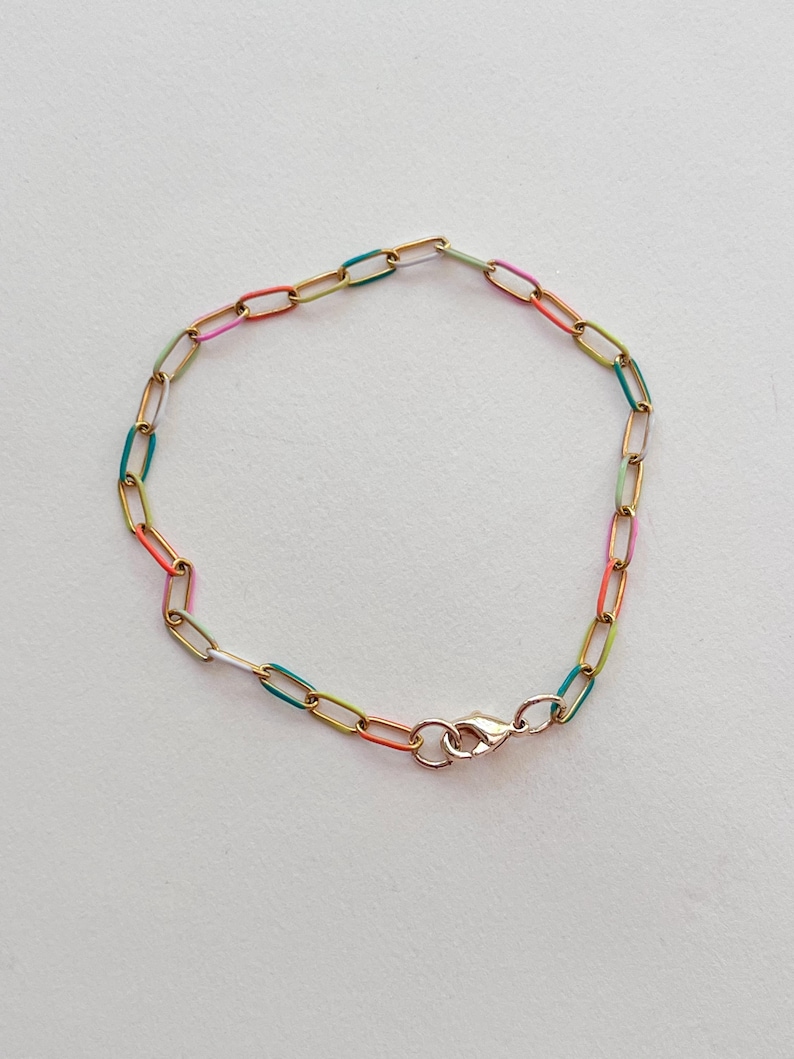 May include: A gold-colored chain bracelet with colorful enamel links in shades of pink, orange, green, and blue. The bracelet has a lobster clasp closure. The jewelry is displayed on a white background.