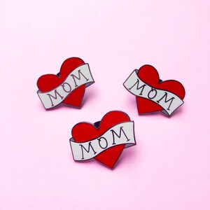 May include: Three red heart-shaped pins with white banners that say "MOM" on a pink background.