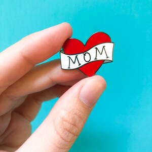 May include: A red heart with a white banner that says "MOM" on it. The heart is a pin.