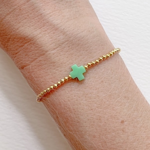 May include: A gold beaded bracelet with a light green cross charm.