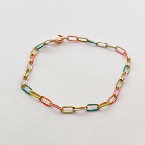 May include: A gold-toned chain bracelet with colorful enamel accents. The bracelet features a series of rectangular links, each partially coated in a different bright color, including pink, orange, green, and blue. The clasp is a heart shape.