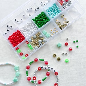 May include: A clear plastic storage box filled with colorful beads, letters, and charms for making bracelets. The box includes red, white, green, blue, silver, and gold beads, as well as star and heart charms. The letters spell out "Merry" and "Santa".