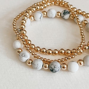 May include: Three gold beaded bracelets with white and gray marble beads.