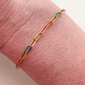 May include: A gold-toned chain bracelet with colorful enamel links. The bracelet features a series of oval-shaped links in a variety of colors, including orange, pink, white, green, and blue. The bracelet is approximately 7 inches in length.