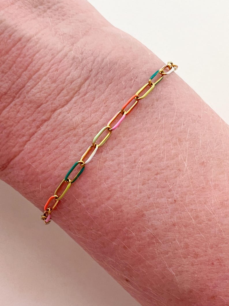 May include: A gold-toned chain bracelet with colorful enamel links. The bracelet features a series of oval-shaped links in a variety of colors, including orange, pink, white, green, and blue. The bracelet is approximately 7 inches in length.