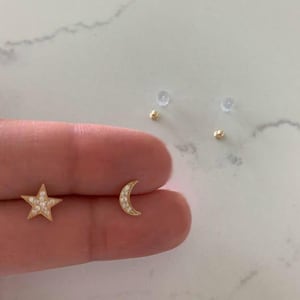 May include: A pair of gold earrings with a star and crescent moon design. The earrings are set with small, clear stones.