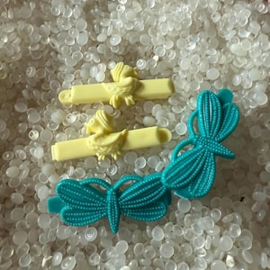 May include: Three plastic hair clips, two yellow clips with a bird design and one turquoise clip with a dragonfly design.