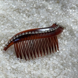 May include: A brown tortoiseshell hair comb with a row of clear rhinestones along the top edge.