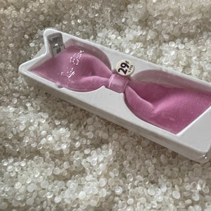 May include: A pink velvet bow tie with a silver clip, packaged in a clear plastic box. The box has a price tag that says "29¢".