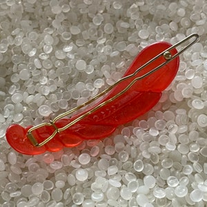 May include: A red lobster-shaped hair clip with a gold-colored metal clasp. The clip is made of translucent plastic and features detailed carving. The hair accessory is designed to hold hair in place.